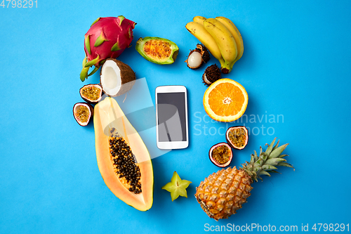 Image of exotic fruits around smartphone on blue background