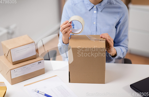 Image of woman packing parcel box with adhesive tape