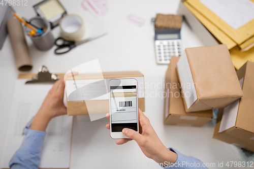 Image of hands with smartphone scans barcode on parcel box