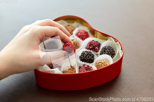 Image of hand with candies in heart shaped chocolate box