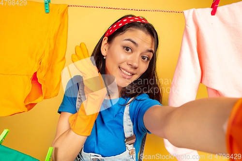 Image of Funny and beautiful housewife doing housework on yellow background