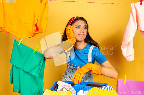 Image of Funny and beautiful housewife doing housework on yellow background