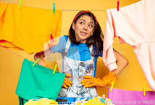 Image of Funny and beautiful housewife doing housework on yellow background