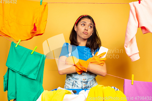 Image of Funny and beautiful housewife doing housework on yellow background