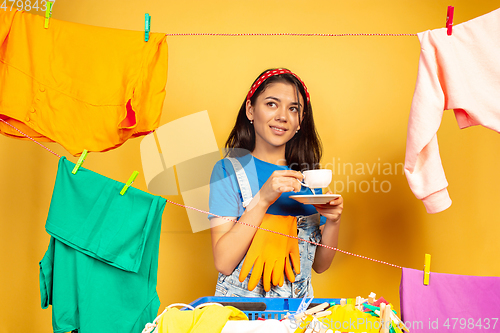 Image of Funny and beautiful housewife doing housework on yellow background