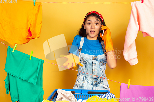 Image of Funny and beautiful housewife doing housework on yellow background