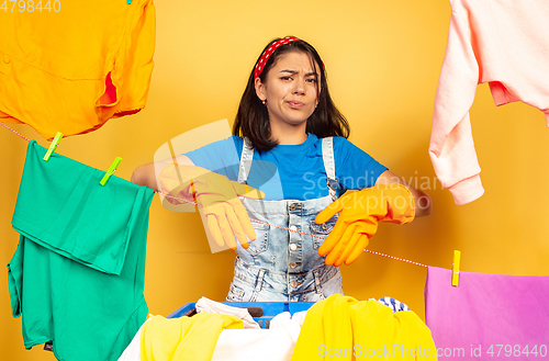 Image of Funny and beautiful housewife doing housework on yellow background