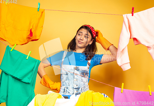 Image of Funny and beautiful housewife doing housework on yellow background