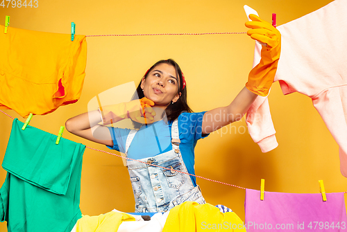 Image of Funny and beautiful housewife doing housework on yellow background