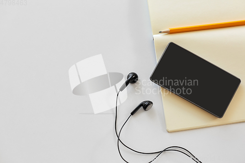 Image of earphones, smartphone and notebook with pencil