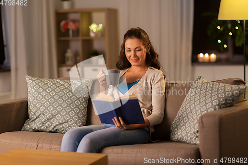 Image of young woman reading book at home in evening