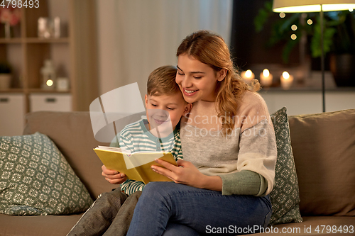 Image of happy mother and son reading book sofa at home