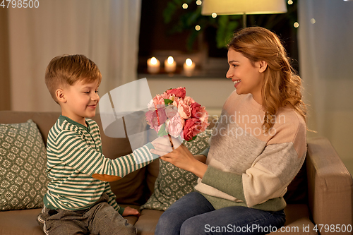 Image of smiling little son gives flowers to mother at home