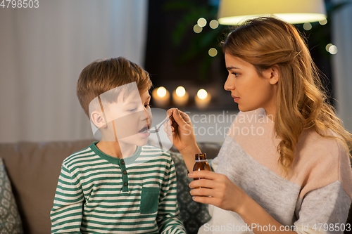 Image of mother giving medication or cough syrup to ill son