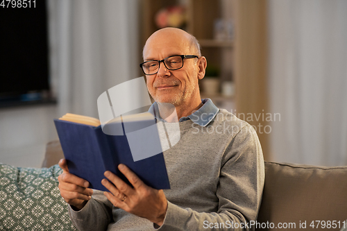 Image of happy bald senior man on sofa reading book at home
