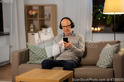 Image of senior man with smartphone and headphones at home