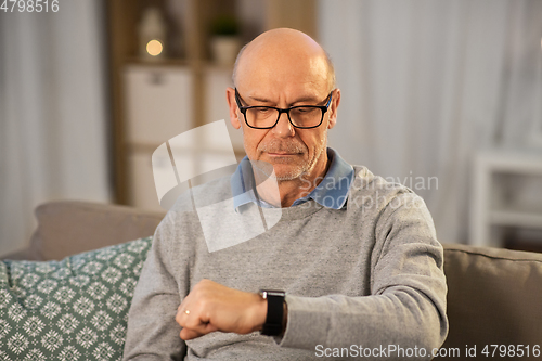 Image of senior man looking at wristwatch at home