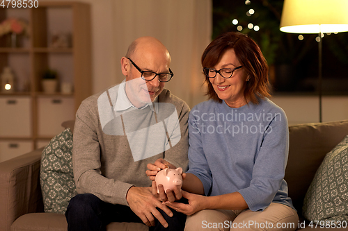 Image of happy senior couple with piggy bank at home