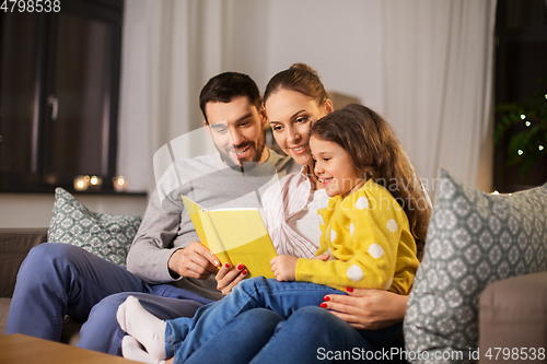 Image of happy family reading book at home at night