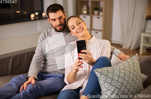 Image of happy couple with smartphone taking selfie at home