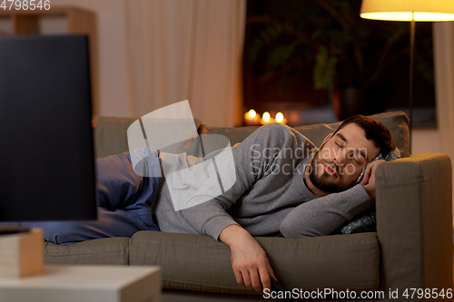 Image of man sleeping on sofa with tv remote at home