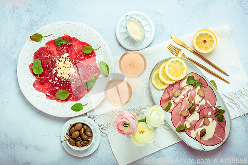 Image of Appetizers - Vitello tonnato and beef Carpaccio with two glasses of rose wine