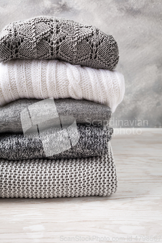 Image of Stack of cozy knitted sweaters and pullovers on wooden background. 