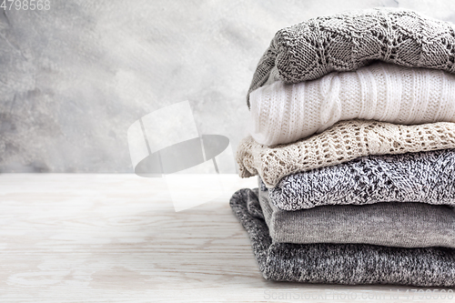 Image of Stack of cozy knitted sweaters and pullovers on wooden background. 