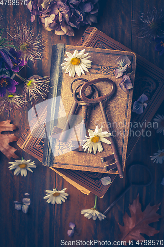 Image of Key to knowledge concept. Old keys on a vintage book with flowers on wooden background