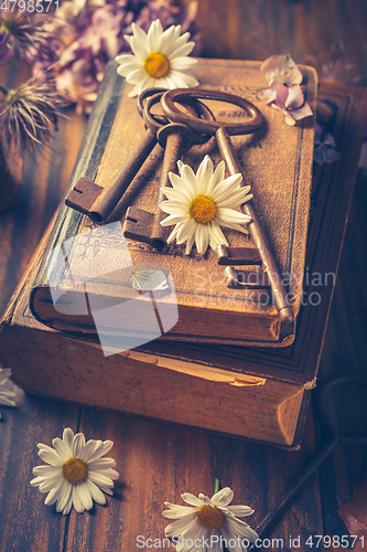 Image of Key to knowledge concept. Old keys on a vintage book with flowers on wooden background