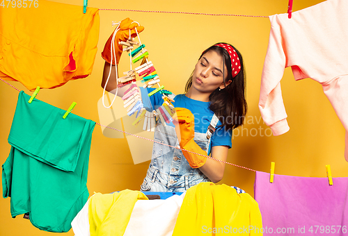 Image of Funny and beautiful housewife doing housework on yellow background