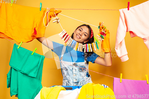 Image of Funny and beautiful housewife doing housework on yellow background