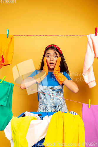 Image of Funny and beautiful housewife doing housework on yellow background