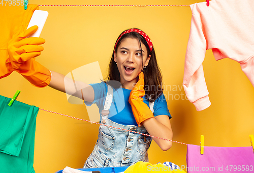 Image of Funny and beautiful housewife doing housework on yellow background