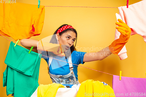 Image of Funny and beautiful housewife doing housework on yellow background