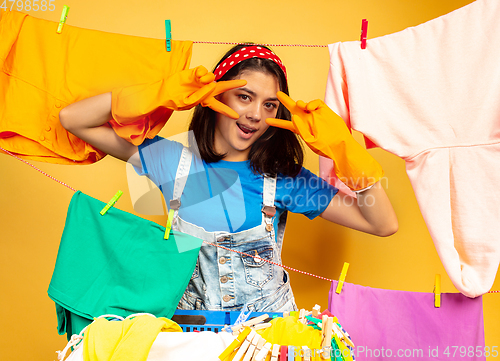 Image of Funny and beautiful housewife doing housework on yellow background