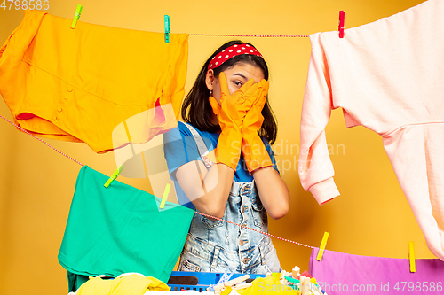 Image of Funny and beautiful housewife doing housework on yellow background