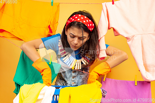 Image of Funny and beautiful housewife doing housework on yellow background