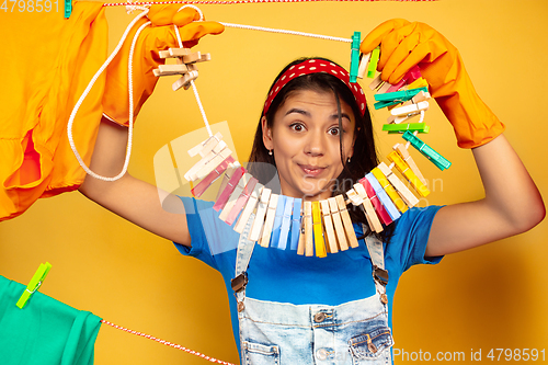 Image of Funny and beautiful housewife doing housework on yellow background