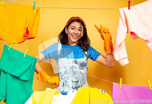Image of Funny and beautiful housewife doing housework on yellow background