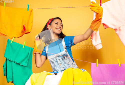 Image of Funny and beautiful housewife doing housework on yellow background