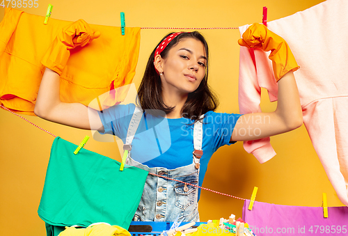 Image of Funny and beautiful housewife doing housework on yellow background