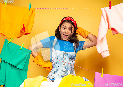 Image of Funny and beautiful housewife doing housework on yellow background