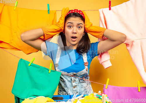 Image of Funny and beautiful housewife doing housework on yellow background