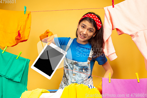 Image of Funny and beautiful housewife doing housework on yellow background