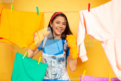 Image of Funny and beautiful housewife doing housework on yellow background