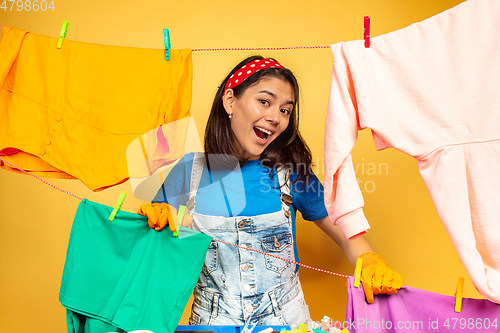 Image of Funny and beautiful housewife doing housework on yellow background