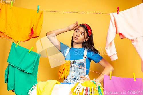 Image of Funny and beautiful housewife doing housework on yellow background