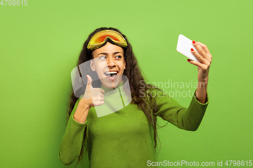 Image of African-american young woman\'s portrait in ski mask on green background