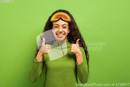 Image of African-american young woman\'s portrait in ski mask on green background